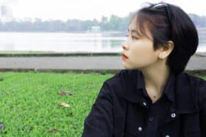 asian teen with short black hair sitting on green grass looking away from camera wearing black button down