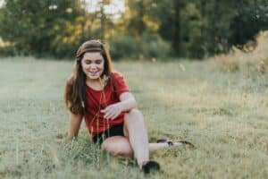 teen girl in red t shirt sitting in grassy field practicing mindfulness outdoors as a coping mechanism