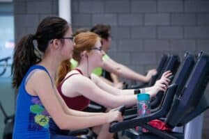 two teen girls working out riding stationary bikes at the gym