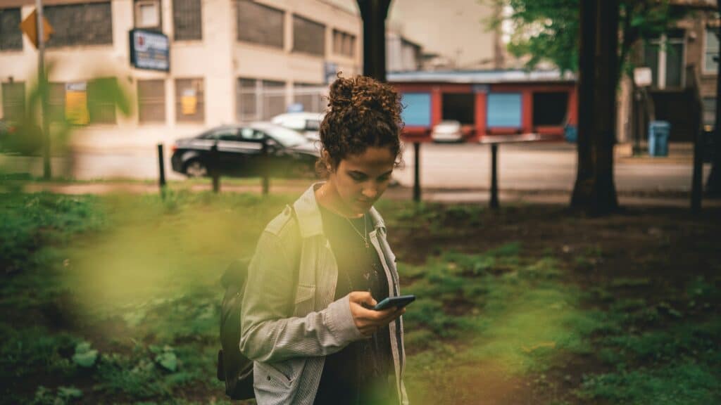 a woman standing in the grass looking at-her cell phone