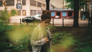 a woman standing in the grass looking at-her cell phone