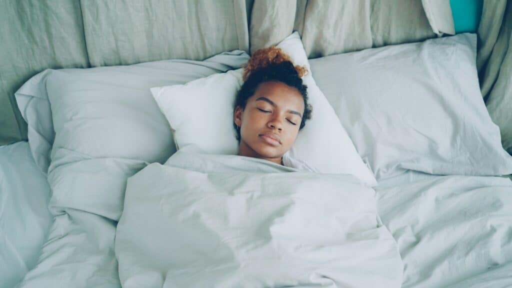teenager sleeping in a bed with white pillows and bedding