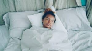 teenager sleeping in a bed with white pillows and bedding